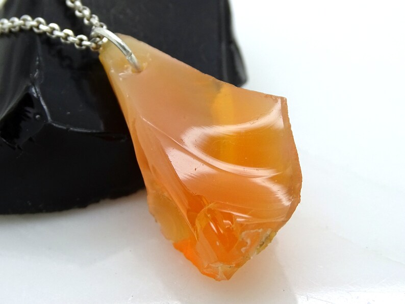 May include: A pendant necklace featuring a large, orange, raw opal stone. The opal is set in a silver bail and hangs from a silver chain.