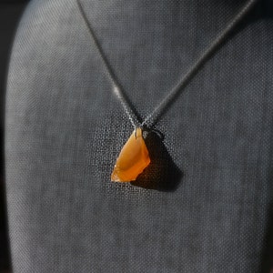 May include: A silver chain necklace with a pendant made of a large, orange, irregular shaped stone.