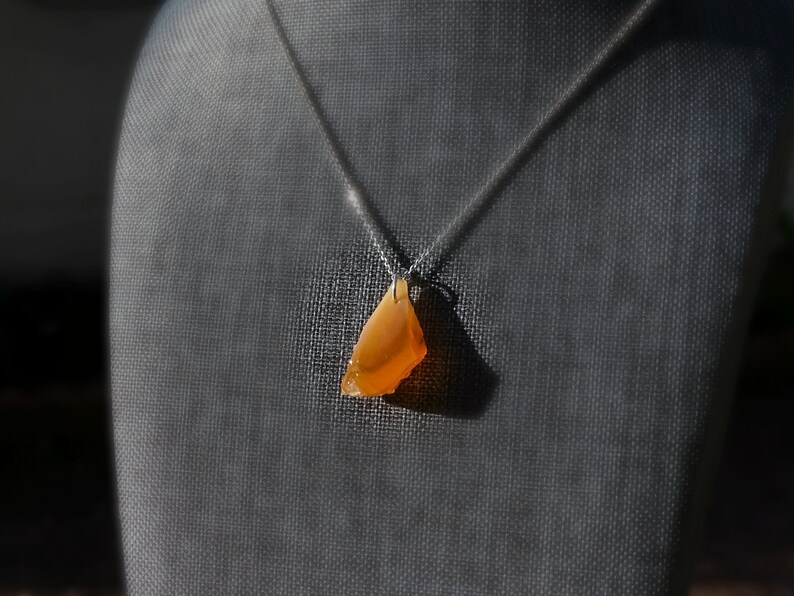 May include: A silver chain necklace with a pendant made of a large, orange, irregular shaped stone.