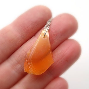 May include: A silver chain necklace with a pendant made of a large, orange, irregularly shaped piece of opal.