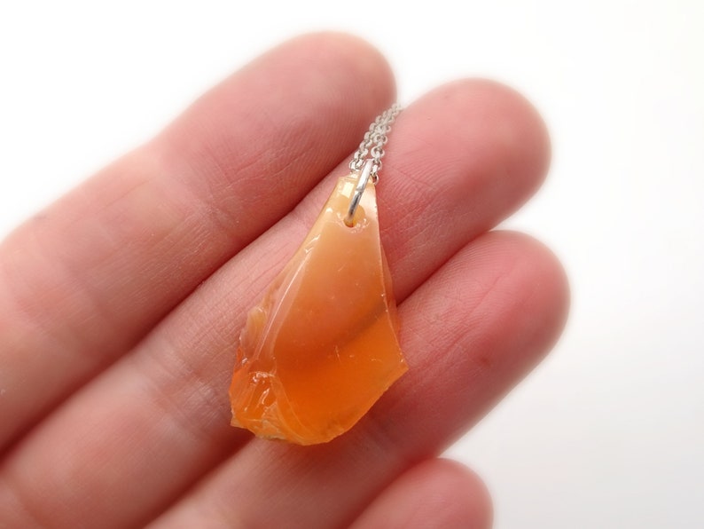 May include: A silver chain necklace with a pendant made of a large, orange, irregularly shaped piece of opal.