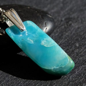 May include: A turquoise blue gemstone pendant with a silver bail. The pendant is on a black surface.