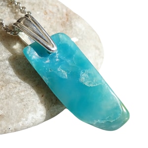 May include: A turquoise blue gemstone pendant on a silver chain. The pendant is a long, thin, irregular shape.