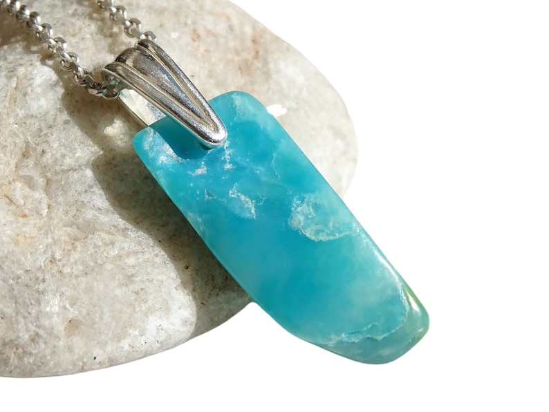 May include: A turquoise blue gemstone pendant on a silver chain. The pendant is a long, thin, irregular shape.