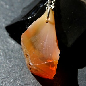 May include: A pendant necklace featuring a raw, orange and white agate gemstone. The agate is attached to a silver chain.
