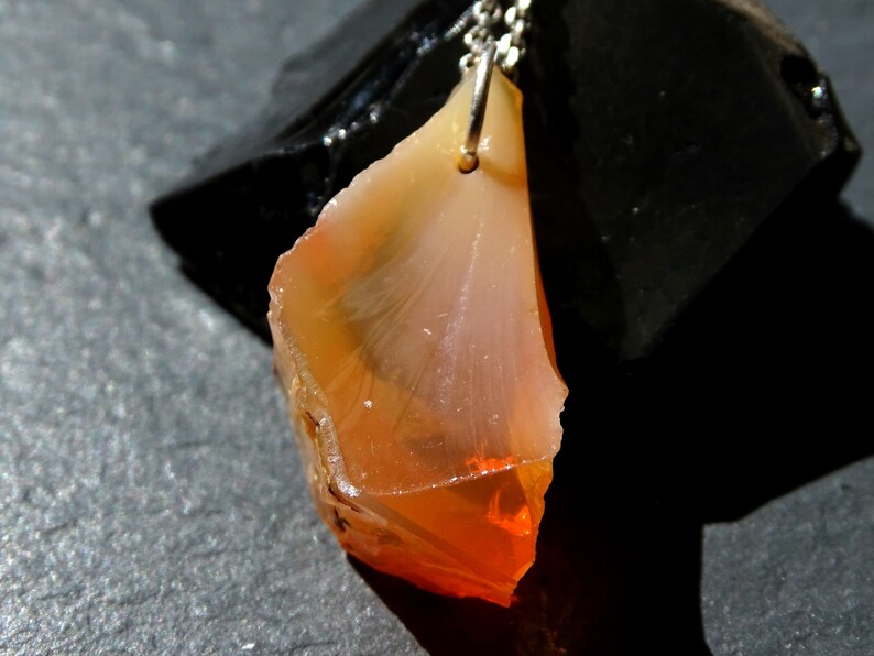 May include: A pendant necklace featuring a raw, orange and white agate gemstone. The agate is attached to a silver chain.