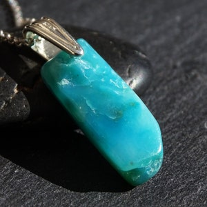 May include: A turquoise blue gemstone pendant on a silver chain. The pendant is a long, rectangular shape with a smooth, polished surface.