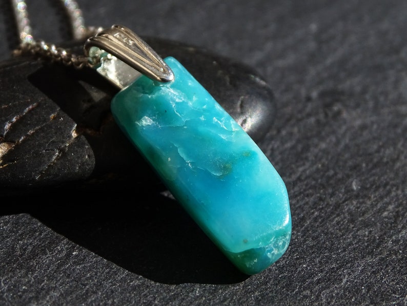 May include: A turquoise blue gemstone pendant on a silver chain. The pendant is a long, rectangular shape with a smooth, polished surface.