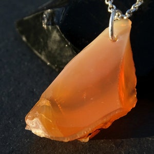 May include: A pendant necklace featuring a large, orange, irregularly shaped opal stone. The stone is set in a silver bail and hangs from a silver chain.