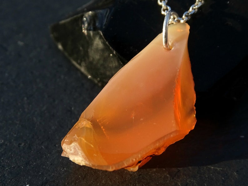 May include: A pendant necklace featuring a large, orange, irregularly shaped opal stone. The stone is set in a silver bail and hangs from a silver chain.