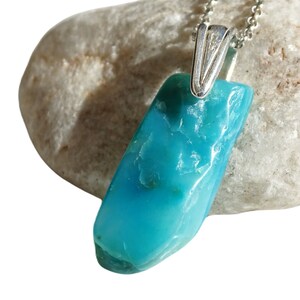 May include: A turquoise blue gemstone pendant on a silver chain. The pendant is a rough, natural shape and is hanging from a silver bail.