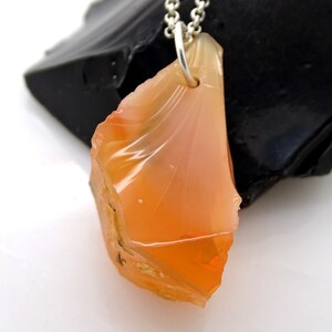 May include: A pendant necklace featuring a raw, orange-colored opal gemstone with a silver chain. The opal is a rough, irregular shape with a translucent, glassy appearance.