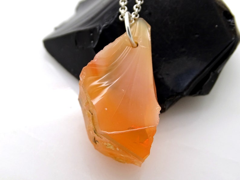 May include: A pendant necklace featuring a raw, orange-colored opal gemstone with a silver chain. The opal is a rough, irregular shape with a translucent, glassy appearance.