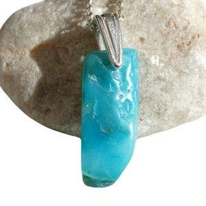May include: A turquoise blue gemstone pendant with a silver bail. The pendant is on a white rock.