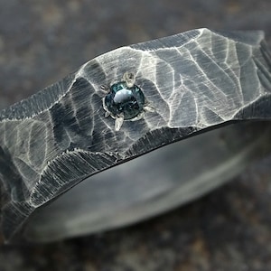 May include: A silver ring with a textured, hammered finish and a single, dark blue gemstone set in the center.