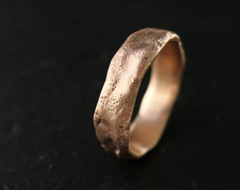 May include: A simple, rustic-style wedding band made of rose gold. The band has a textured, hammered finish and a slightly irregular shape.