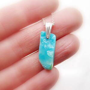 May include: A silver chain necklace with a light blue and white gemstone pendant. The pendant is a natural, irregular shape.