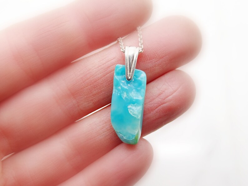 May include: A silver chain necklace with a light blue and white gemstone pendant. The pendant is a natural, irregular shape.