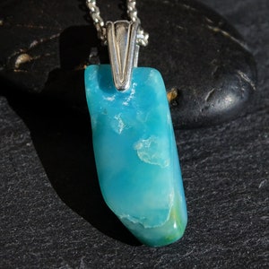 May include: A pendant necklace featuring a light blue, irregularly shaped gemstone with a silver bail.