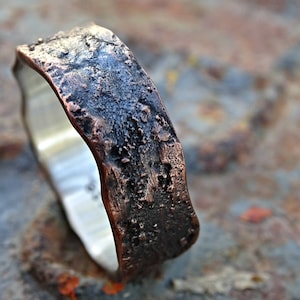 May include: A rustic copper ring with a textured, hammered finish. The ring is wide and has a slightly irregular shape.