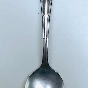 May include: A silver spoon with an ornate handle and a rounded bowl. The handle features detailed scrollwork and a decorative design at the top. The spoon is likely vintage or antique, and is made of a shiny, reflective metal.