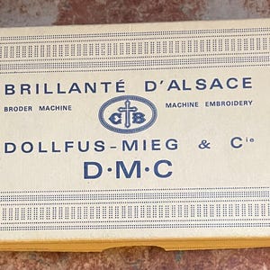May include: A rectangular box with the text "BRILLANTÉ D'ALSACE" and "DOLLFUS-MIEG & Cie D.M.C" in blue. The box has a decorative border and a red circle with "Art. 237".