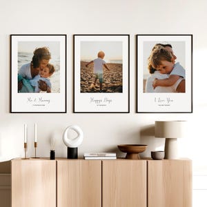 May include: Three black framed photos with white mats and white text on a white wall. The photos show a mother and child on the beach, a child walking on the beach, and a father and child hugging. The text on the photos reads "Me & Mummy", "Happy Days at the Beach", and "I Love You You Are the Best".