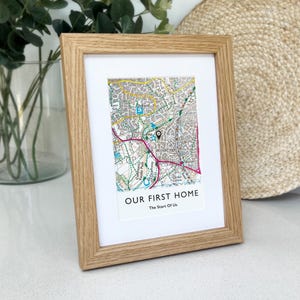 May include: A framed map print in a light oak frame. The map features a detailed street layout with a pin marking a location. The text "OUR FIRST HOME" and "The Start Of Us" are printed below the map, making it a personalized gift.