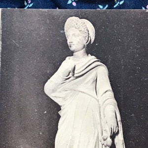 Puede incluir: Fotografía en blanco y negro de una estatua de mármol de una mujer con una túnica larga y un tocado. La estatua está expuesta en un museo. El texto de la postal dice: "104 NIMES. Musée de la Maison Carrée. Julie, fille de Tilus, trouvée à Bouillargues (Gard), en 1840. - ND."