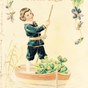 Antike 1900er Jahre Geburtstag leicht geprägte Postkarte, kleiner Junge gekleidet in Blau Sammeln lila Blumen in seinem Ruderboot