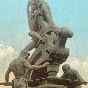 May include: A bronze sculpture of three figures working on a large wheel. The figures are nude and appear to be in a state of exertion. The sculpture is set against a blue sky with white clouds.