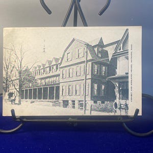 May include: Black and white vintage postcard showing a large, multi-story building with a porch. The building is labeled "Assabet and Middlesex Houses, Maynard, Mass."