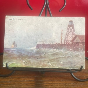 May include: Vintage postcard depicting a lighthouse on a rocky shore with a sailboat in the distance. The postcard is titled "The Breakwater" and has a copyright date of 1904.