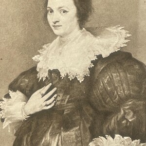 May include: A black and white portrait of a woman wearing a large white lace collar and a dark dress. She is holding her hand to her chest and is wearing a ring on her finger.