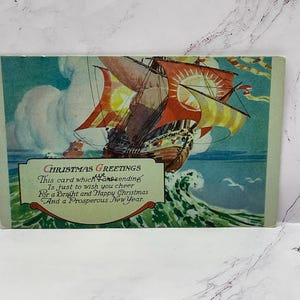 May include: Vintage Christmas card depicting a sailing ship at sea with red and yellow sails. The card includes the text "Christmas Greetings" and a festive message for the holiday season.