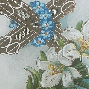 Op de afbeelding: Een vintage paaskaarten met een bruin kruis met gouden accenten, omringd door blauwe vergeet-mij-nietjes en witte lelies.