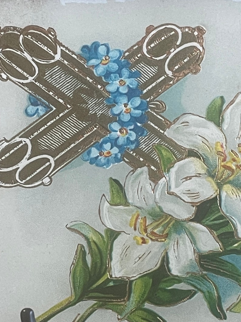Op de afbeelding: Een vintage paaskaarten met een bruin kruis met gouden accenten, omringd door blauwe vergeet-mij-nietjes en witte lelies.