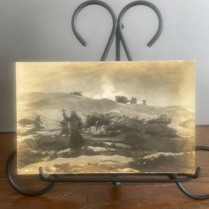 May include: A vintage black and white postcard depicting a group of people pulling a wagon in a snowy landscape.