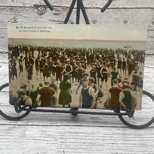 May include: Vintage postcard with a black and white photo of a large crowd of people on a beach. The text on the postcard reads "$5.00 Reward if you find me in this Crowd of Bathers."
