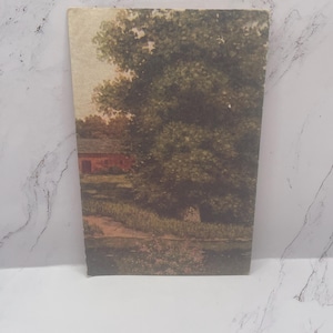 May include: A rectangular vintage print featuring a landscape scene. The artwork depicts a red building, lush green trees, and a body of water. The print has a slightly aged appearance, with visible wear on the edges.