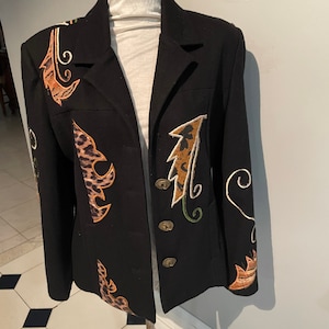 May include: Black blazer with decorative leopard print and leaf-like designs in shades of brown, orange, and green. The blazer has three gold-colored buttons and is displayed on a mannequin.