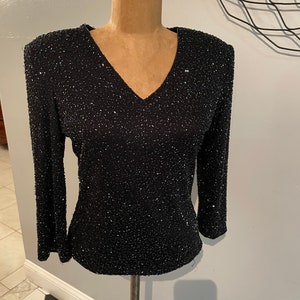 May include: A black sequined top with a v-neck and long sleeves.