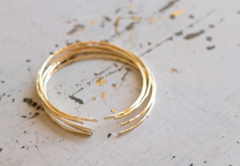 Stack on 14k gold-filled hammered open cuff bangles, 18 gauge wire hand hammered, hand polished, stacked on white table in L.A.Osborn Studio