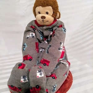 May include: A plush monkey toy wearing a gray and red fleece sleeper with a fire truck and ambulance print. The sleeper has a zipper closure and the monkey has brown fur.