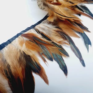 Peut inclure: Une garniture de plumes brunes, noires et vertes avec un dos de ruban noir. Les plumes sont de différentes longueurs et sont disposées en cascade.