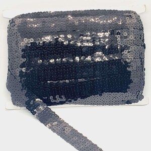 May include: Black sequined trim with a shiny finish. The trim is made of small, round sequins that are sewn together in rows. The trim is approximately 2.5 cm wide.