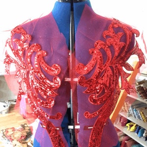 Op de afbeelding: Rode pailletten-kant applique met een bloemenmotief. De applique is op een rood gaasstof en is perfect om een ​​toets van glitter toe te voegen aan elk project.