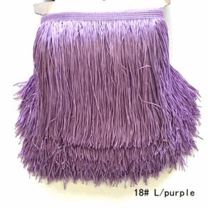 May include: A light purple fringe trim featuring a woven header band with long, straight, hanging strands. The trim is layered to create a full, textured appearance. The text 18# L/purple is printed in the bottom right corner of the image.