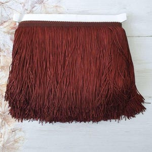 May include: A close-up of a deep red fringe trim. The fringe is made of thin, soft fibres and is approximately 2.5 cm wide.