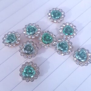 May include: Ten green and clear rhinestone flower embellishments with gold settings.